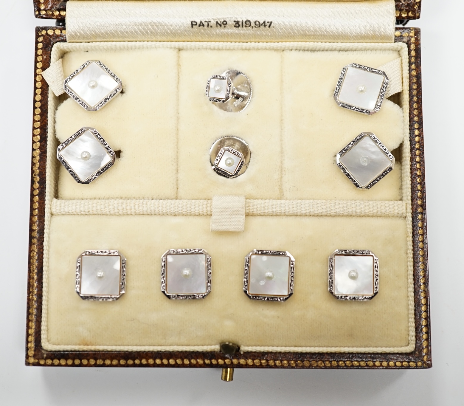 A 9ct white metal, mother of pearl and seed pearl set eight piece dress stud set, in fitted gilt tooled leather case.